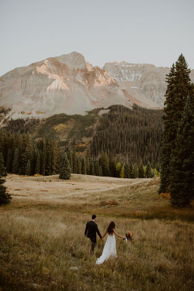 Bride and groom walk through Telluride mountains