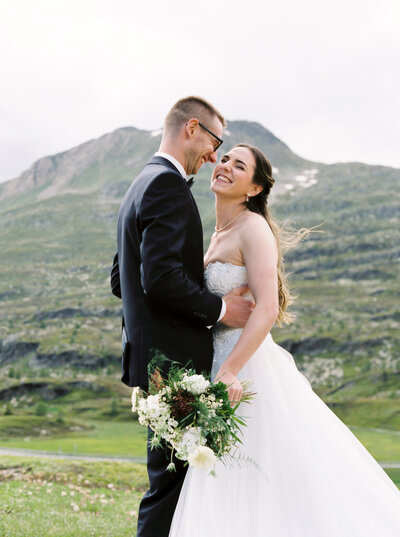 Bride and groom smile with wedding bouquet next to mountain