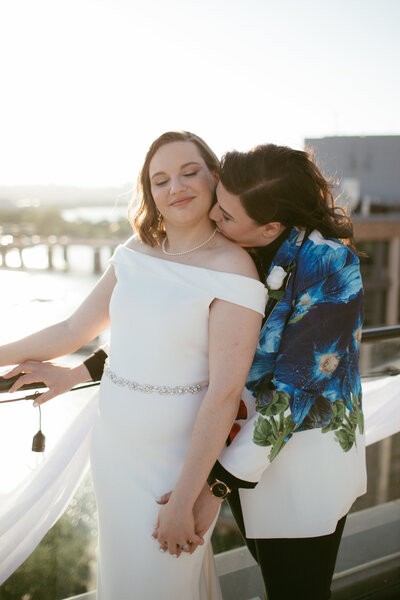 bride and bride on a terrace overlooking the anacostia river with bride kissing bride's neck