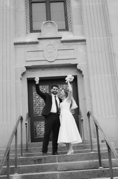 Black and white photo of a bride and groom celebrating their civil ceremony as they walk out of the courthouse. 