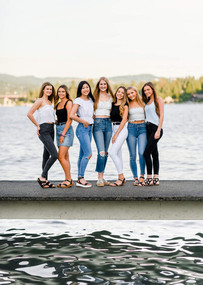 High school senior girls stand on a dock hugging each other at sunset