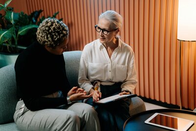 An older white women and younger black women sit and review a piece of paper together