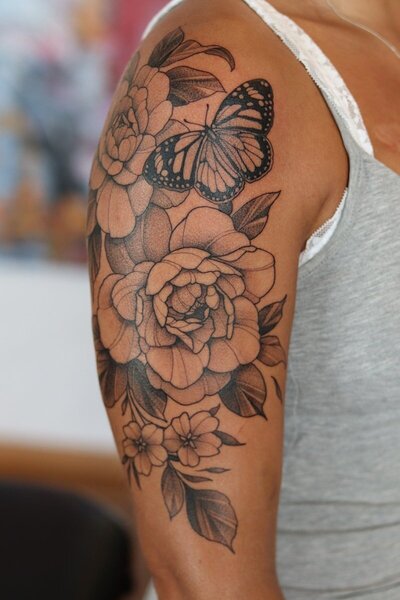 Black and grey tatuering av blomma och blad på arm.