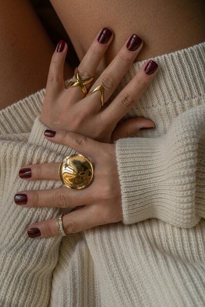 Close-up of a client’s hands with deep red polish and gold jewelry, showcasing a natural nail manicure at Maven + Grace.