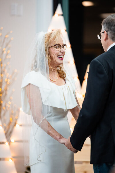 Woman in wedding dress and glasses laughs at her husband during their elopement ceremony.