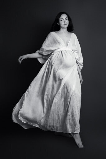 Studio portrait of a pregnant woman in a long white dress.