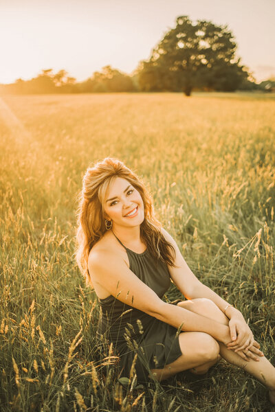 woman sitting in a field wearing a green dress while smiling