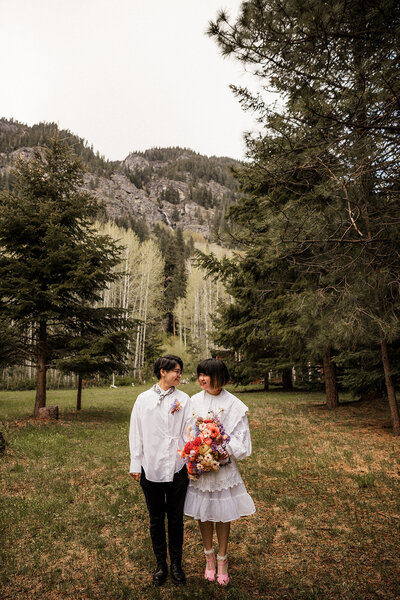 Two brides smiling at each other with pine trees and mountain in the background!