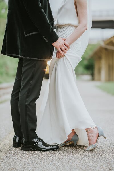 Shoulders down view of bride in floor length dress and groom in velvet suit on road