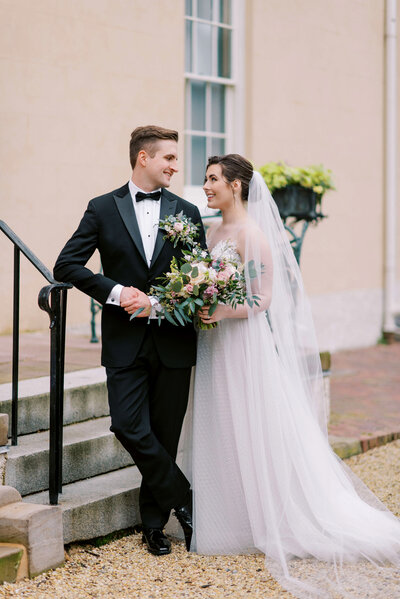 Newly married bride and groom look at each other while leaning against the stairs at their outdoor DC wedding venue