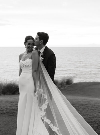 Black and white image of bride and groom sharing a kiss at sunset on the 3rd tee at Mauna Kea Beach Resort, capturing a romantic and timeless moment during their luxury destination wedding in Hawaii