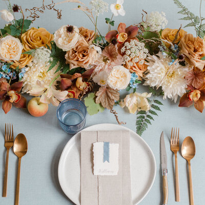 A low table centrepiece of orange roses in front of a place setting.