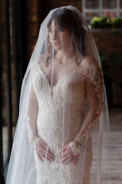 Bride under a veil looks out window at Loft Lucia in Chicago, IL