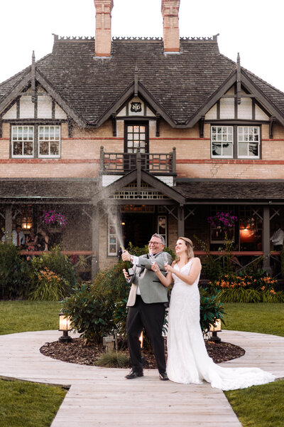 grooms pops a bottle of champange while the bride watches in front of the bow valley ranche restaurant 