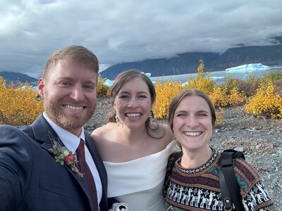 happy elopement couple and photographer smiling at the camera with mountains and glacier in the backgroun