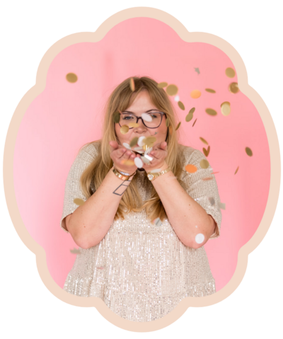 woman with blonde hair wearing silver dress blowing confetti in front of pink background