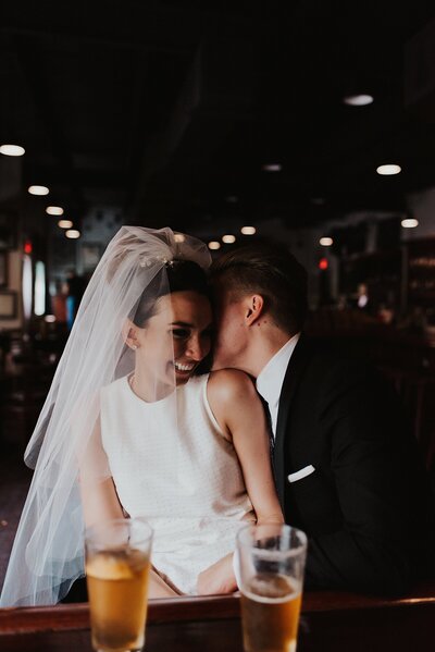Groom whispering in brides ear while they drink beers at a downtown Tampa bar after their ceremony at Le Meridien Tampa