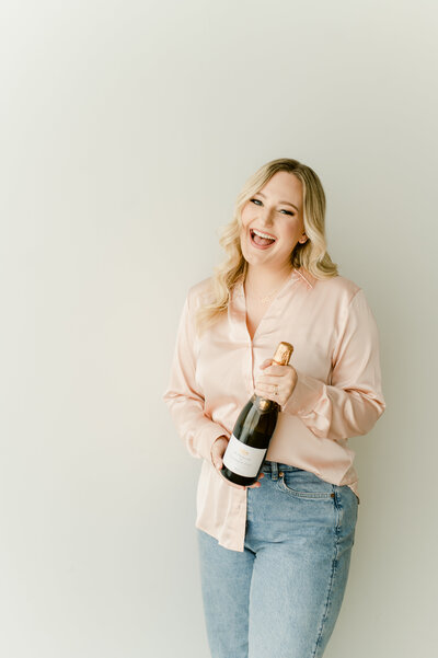 a woman in a pink shirt and jeans holding a champagne bottle