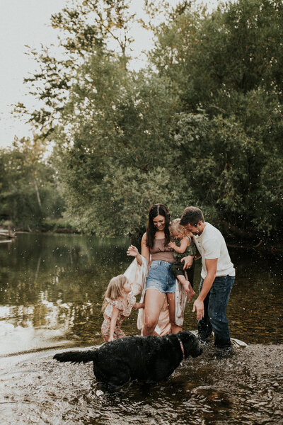 A man and woman look at their children and black lab while playing in a lake