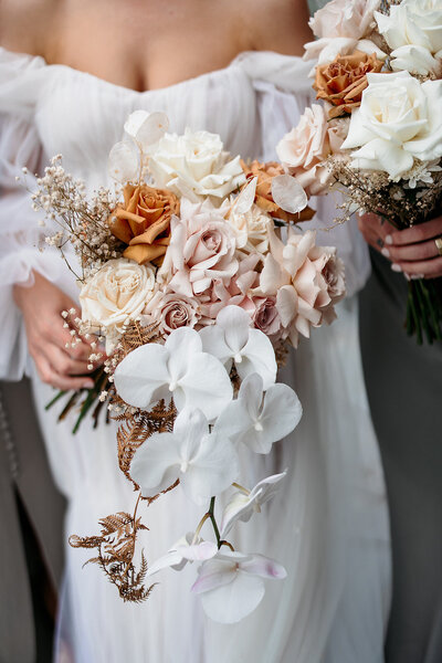 Bridal bouquet of flowers held by bride featuring white phalaenopsis orchid, dusty light pink roses, cream roses, toffee roses and dried flowers