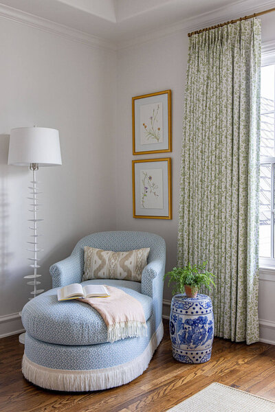 A white kitchen with white chairs and blue upholstered fabric around a white island styled with florals and fruit.