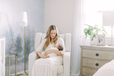 Mother holding newborn baby boy in the nursery sitting in a chair