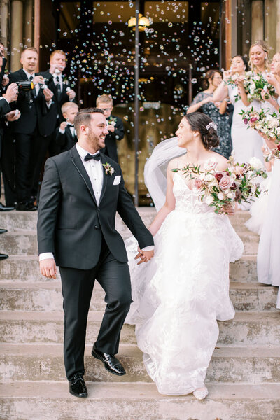 indian groom wearing a black tux and dried floral boutonniere wraps arm around the bride at the brown hotel in louisville in front of a baby breath ceremony arch with pastel flower colors by louisville wedding florist roots floral design