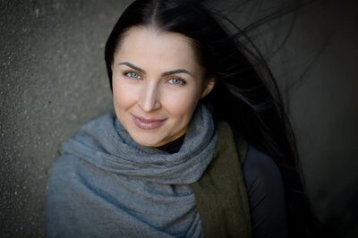 Smiling woman with long dark hair wearing a scarf, outdoor professional headshot in New York City by Alex Kaplan.