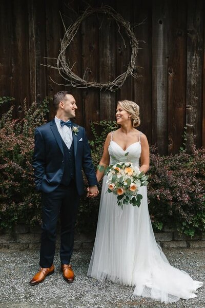 Couple smiling at each other standing in front of a decorate wall at their Seattle wedding.