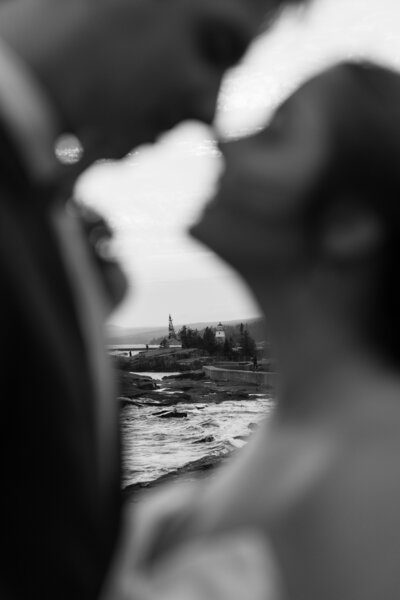 Candid kiss between eloping couple with the lighthouse peeking through the space between them. 