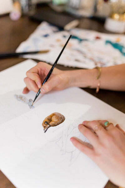 Courtney's hands illustrating a painting of a fox and owl