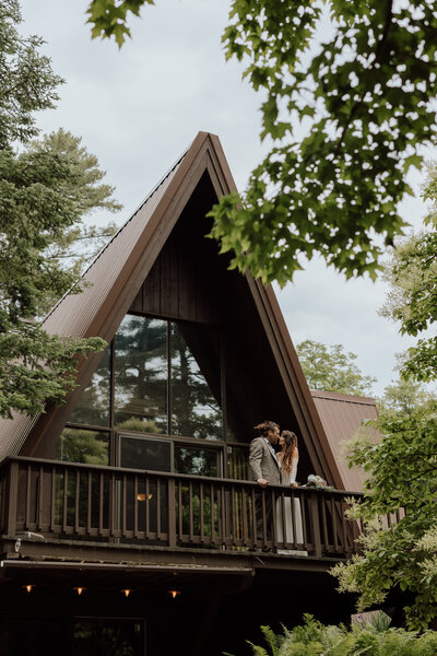 bride and groom standing on the deck of an a-frame cabin.