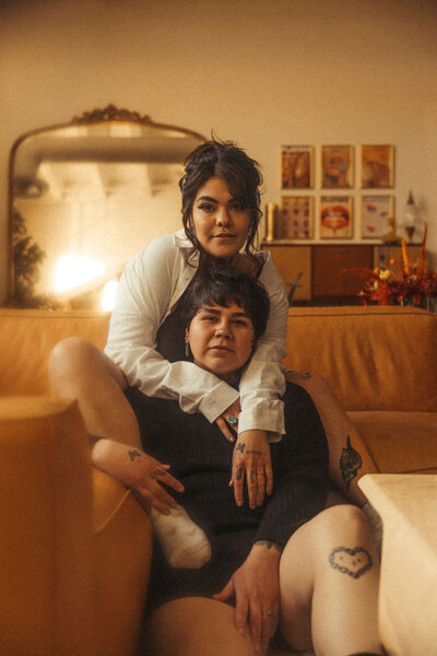 A person sitting on a couch with their leg over their partner's shoulder who is sitting on the ground under them.