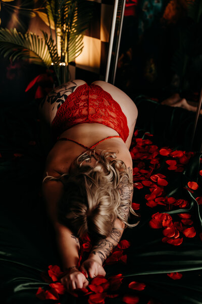 Boudoir photography woman in red lingerie kneeling on bed with black silk sheets and red rose petals in Amarillo TX