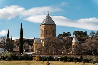 Stone church with a conical metal roof set among cypress trees and rolling hills near Tbilisi | theViatrix Private Georgia Luxury Travel