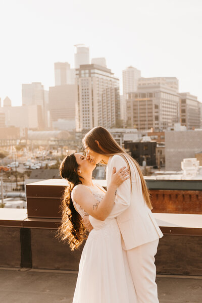 two brides kissing with Minneaoplis skyline in the background 