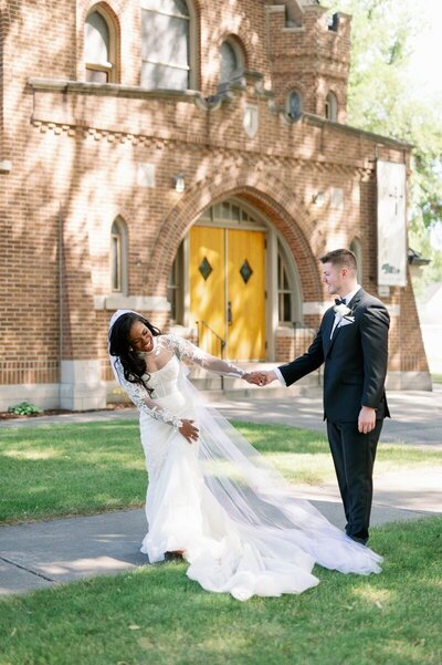 bride and groom holding hands and smiling outside of brick building with yellow doors for minneapoils wedding