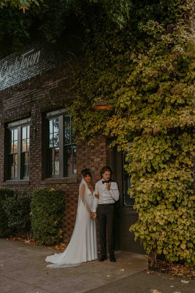 bride and groom standing next to a brick wall with greenery going up the wall in downtown Portland