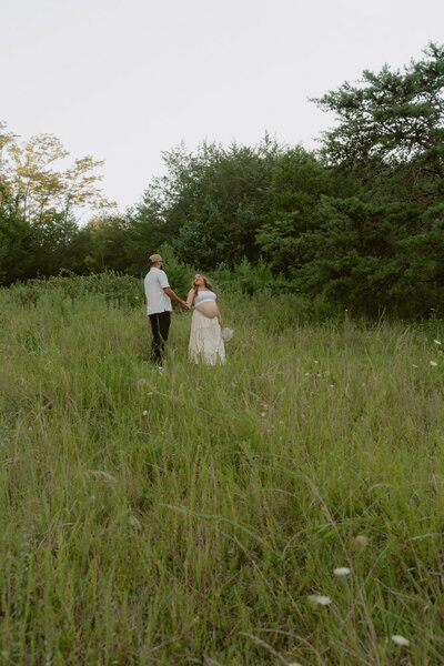 An couple expecting their first baby walk together in a grassy field at Wing Deer Park in Johnson City, TN. Michaela Crawford Photography, a cinematic maternity photographer located in Northeast, TN. 