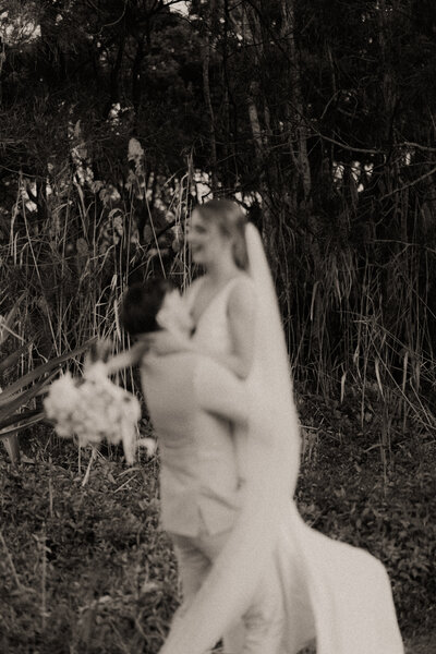 An aesthetic and artistic black and white wedding photo of a Coffs Harbour bride and groom. He is picking her up candidly.