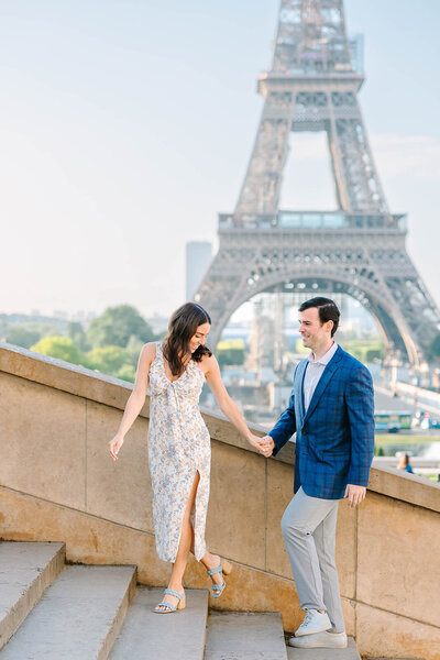Romantic couple walking hand-in-hand up the stairs with the Eiffel Tower in the background during a Paris couples photoshoot.
