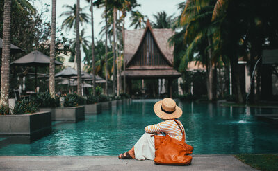 Woman sitting pool side at a Bali style 5 star resort, symbolising enjoying having the Financial means to travel and enjoy the workd.