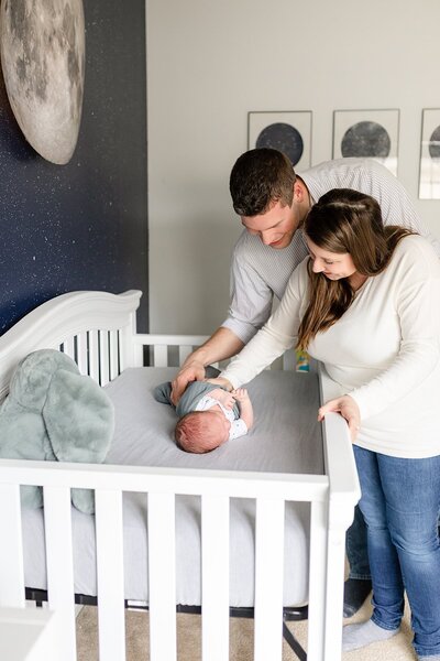Mom and dad looking at newborn baby boy in crib in galaxy nursery