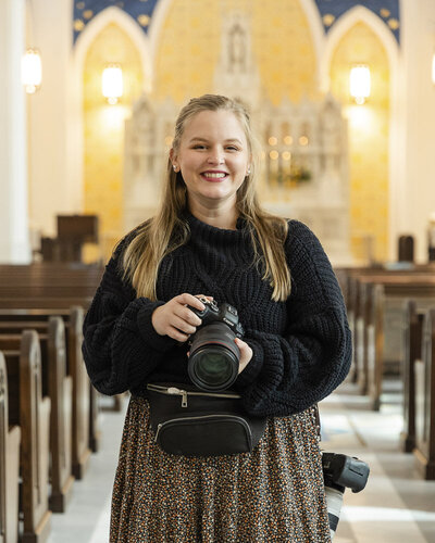 Nicole smiling and holding a camera while standing inside a Catholic church