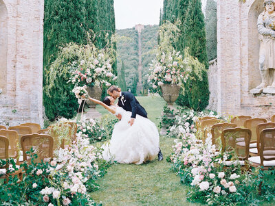 a couple shares a dip kiss in the middle of the aisle after their Tuscany Italy wedding ceremony