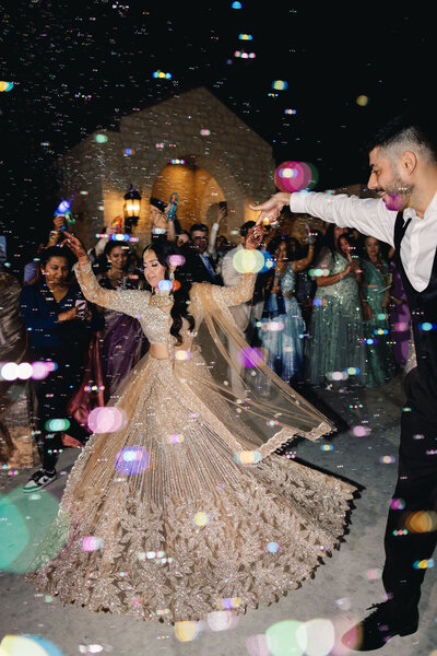 A bride and groom walking through a crowd of people with bubbles around them
