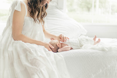Picture of a mother caressing her newborns cheek as they sit on a white bed during session in their Kansas City home