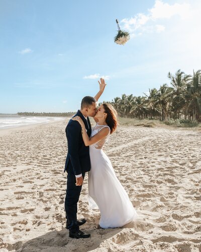 Bride and groom kissing, while bride throws her wedding bouquet