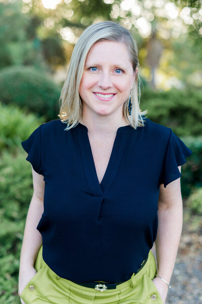 Headshot of Kristin Palkoner of Lens and Prism Personal Branding Photography wearing a black shirt and green pants, smiling.