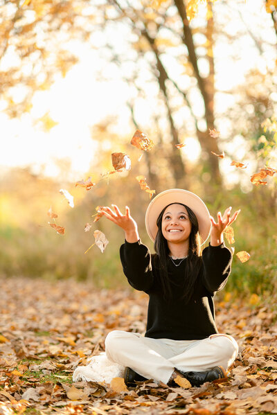 high school senior girl throwing fall leaves in the air for her senior photos